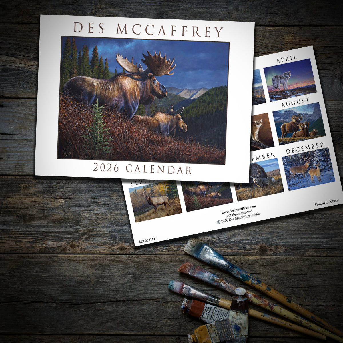 Des McCaffrey 2026 calendar with wildlife artwork on a wooden surface with paintbrushes.