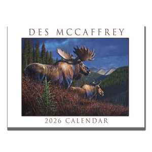 2026 wall calendar by wildlife artist Des McCaffrey featuring a cover illustration of two moose in an autumn mountain landscape, shown on a rustic wooden surface with paintbrushes and tubes of oil paint.