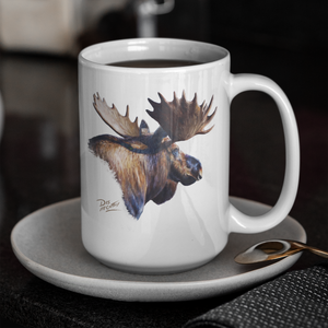White ceramic coffee mug featuring a detailed moose painting by artist Des McCaffrey, displayed on a saucer with a spoon in a café setting.