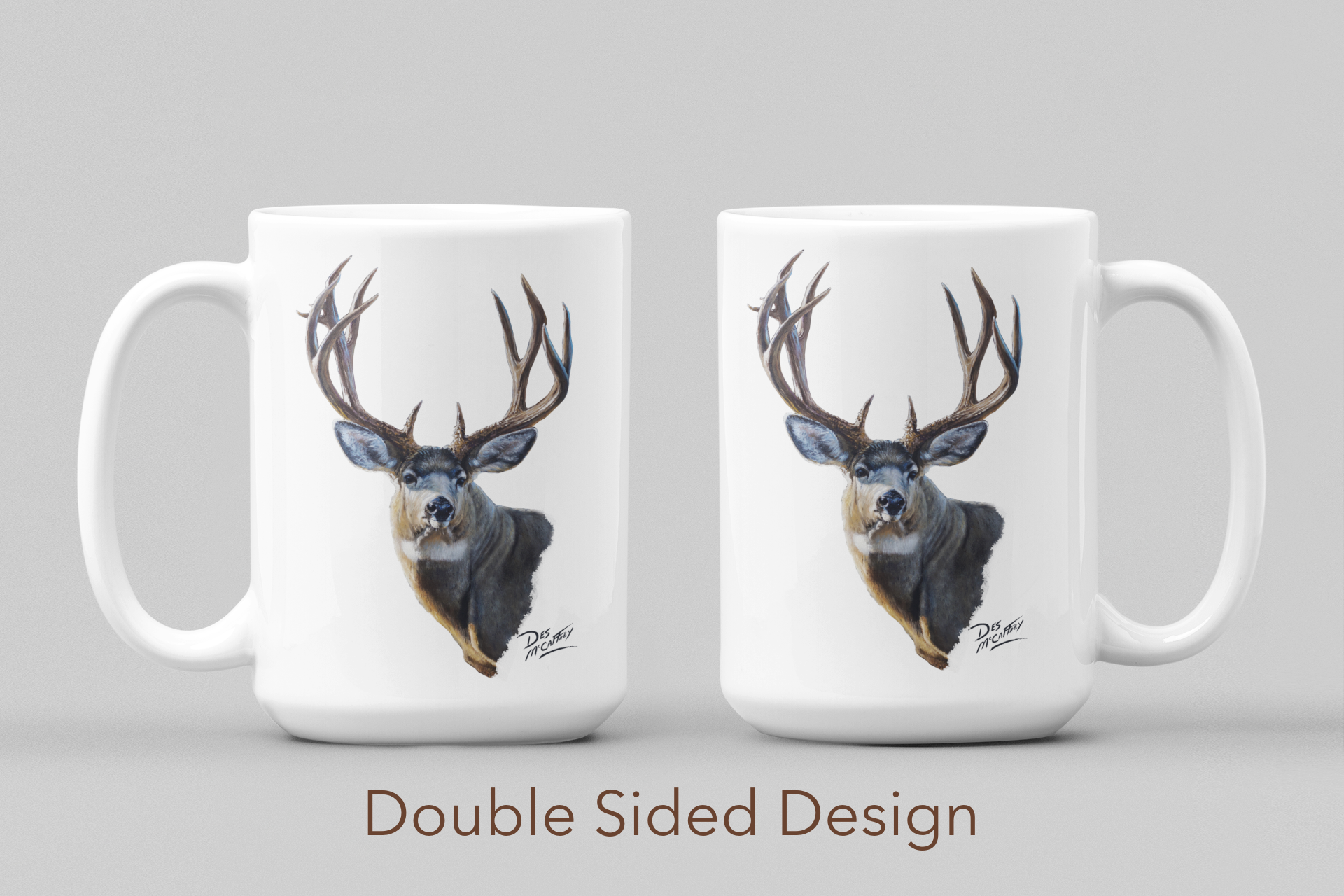 White ceramic coffee mug featuring a painting of a trophy mule buck, artwork by Canadian wildlife artist Des McCaffrey, both sides displayed.