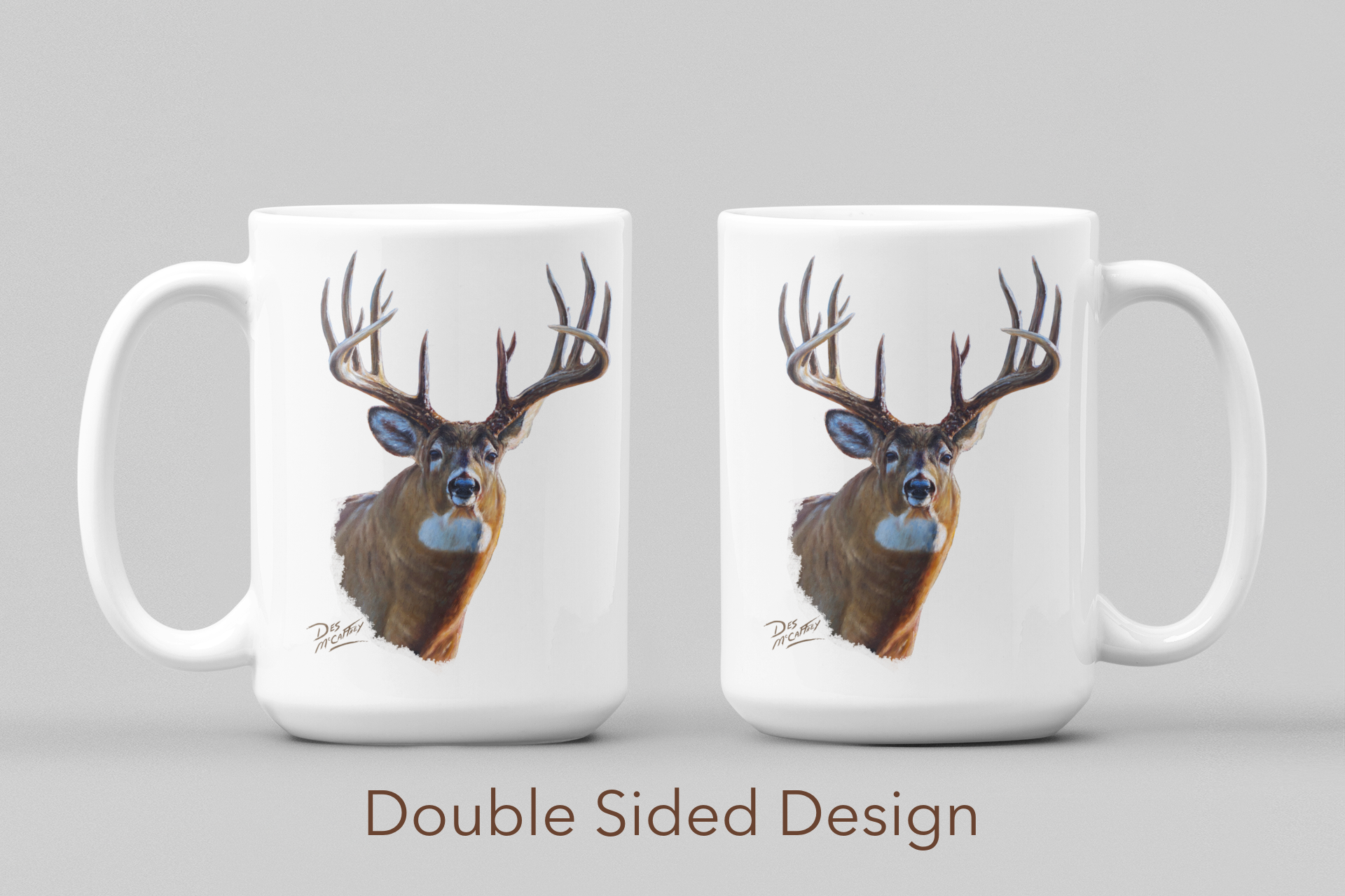 White ceramic coffee mug featuring a painting of a whitetail buck with large antlers, artwork by Canadian wildlife artist Des McCaffrey, displayed on both sides. 